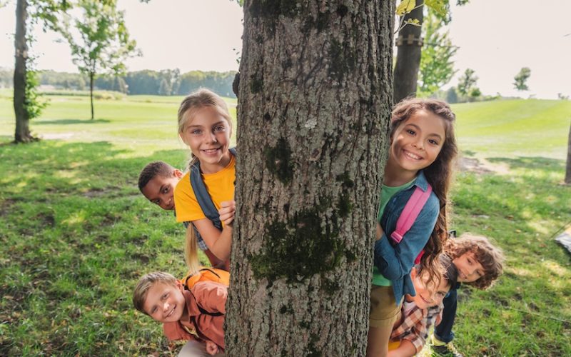 happy multicultural group of kids smiling near tree trunk